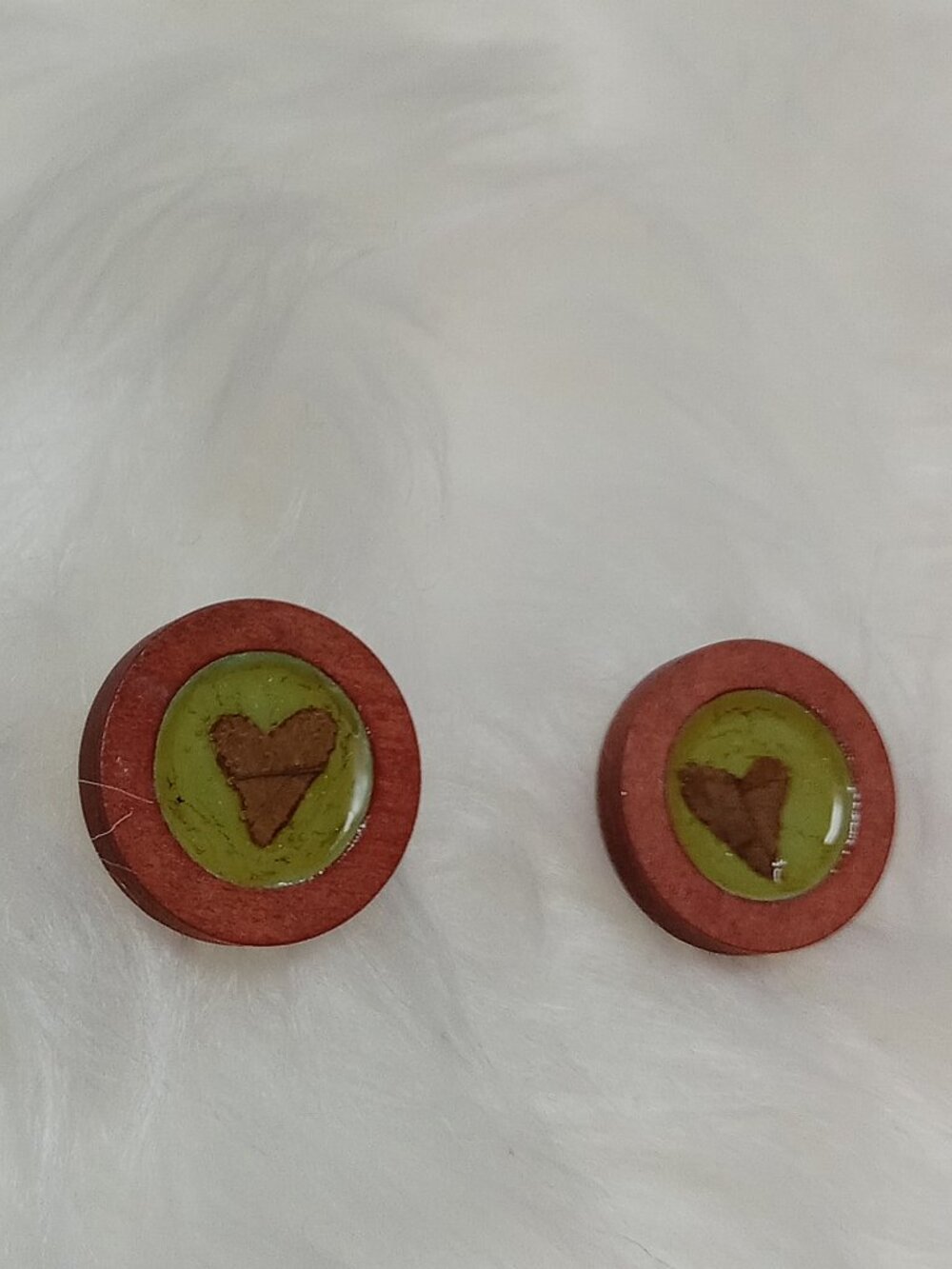 Handmade earrings on a wooden base with a piece of punched-out tree leaf